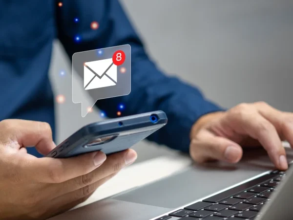 Homem usando um notebook e com um celular na mão direita